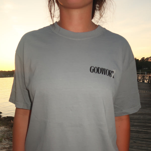 Person wearing a gray t-shirt with a 'GODWORX' logo during a sunset.