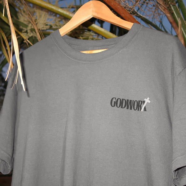 Gray t-shirt with 'GODWORX' logo on a wooden hanger against a natural background