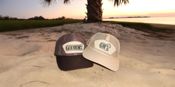 Two godworx caps with logos on a sandy beach at sunset